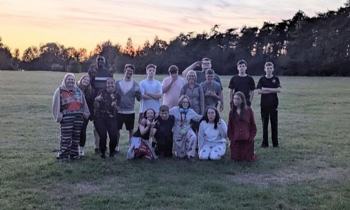 Staff and students on the Duke of Edinburgh expedition posing as a group on a camp side whilst the sun is setting